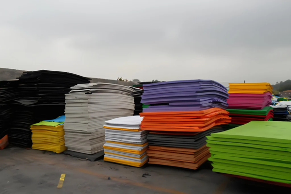 Stacks of colorful EVA foam sheets in various thicknesses, including black, white, orange, purple, and green, stored outdoors in an industrial setting